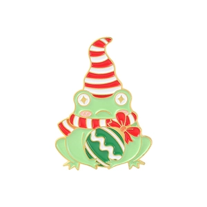 Christmas frog enamel pin wearing a Santa hat and scarf with a festive gift ball ornament
