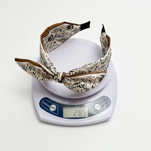 Wide paisley print headband with bow detail on a scale showing product weight