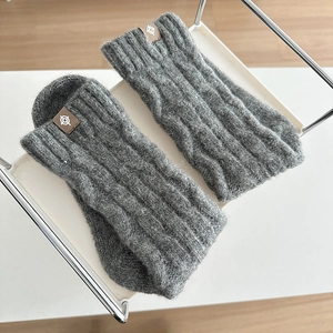 Detail of dark grey cable knit wool leg warmers with brown leather logo patch