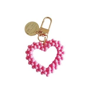 Handmade woven pink pearl heart keychain with golden alloy clip on white background