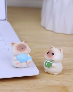 Cute resin Siamese cat figurines with blue fish and drink on a wooden desk