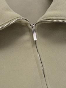Close-up of silver metal zipper and soft fleece fabric texture on a sage green hoodie