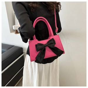 Detail shot of pink handbag featuring a large black satin bow and adjustable long shoulder strap
