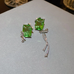 Macro detail of asymmetric bow earrings with green radiant cut stone and silver tassel