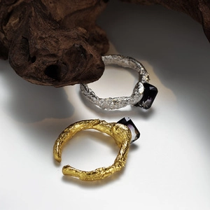 Detailed view of silver and gold textured rings with dark square stones on wood