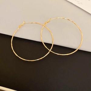 Detailed view of large gold hoop earrings with textured hammered finish on dark background