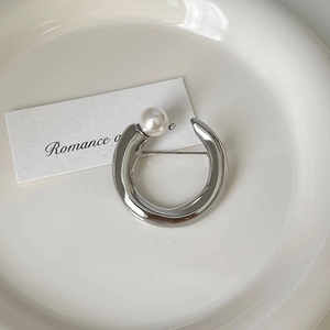Detail of silver stainless steel circular brooch with an elegant white pearl accent