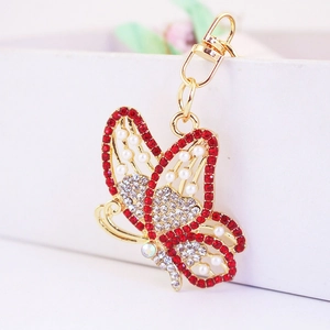 Golden butterfly keychain with red rhinestones and pearls on a white gift box edge