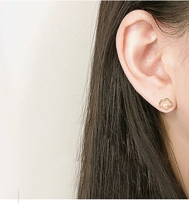 Close-up of cloud shaped gold earring with pink pearl worn by a model in soft light