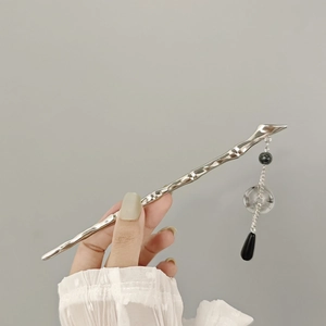 Detailed view of silver fluid textured hair pin with elegant black tassel droplets