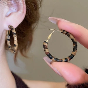 Macro detail of retro C-shaped earrings featuring leopard print leather texture and gold clasp