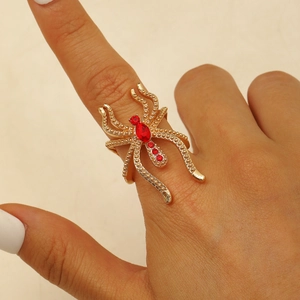 Gros plan d'une bague araignée gothique dorée avec cristaux rouges au doigt