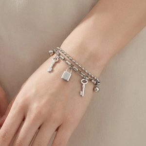 Close-up of silver double-layered bracelet featuring vintage key and padlock pendants