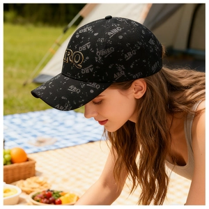 Détail du logo brodé doré sur casquette noire à motif ARQ dans un décor de camping chic