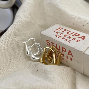Macro shot of minimalist gold and silver U-shaped earrings on rustic linen background