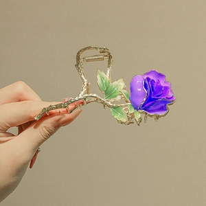 Detail of elegant gold-tone flower hair claw with purple rose and green leaf design