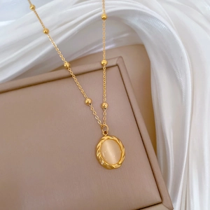 Detail of gold necklace with oval cat eye stone and twisted metal frame on silk fabric