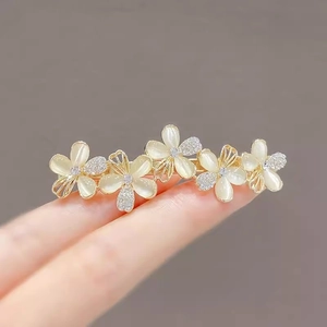 Elegant gold hair clip with five white pearl flowers and rhinestones held on fingers