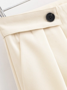 Detailed macro view of the button closure and pleated waist on cream high-waisted trousers