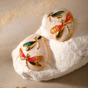 Detail view of oval enamel earrings with gold dragonfly patterns on white marble texture