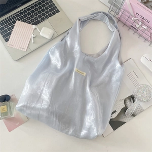 Detailed flat lay of a silver-blue metallic tote bag with lifestyle accessories on a desk