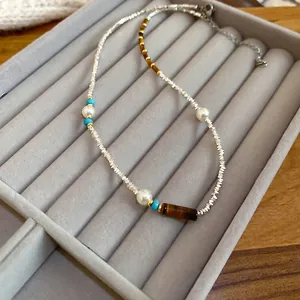 Tiger eye and pearl beaded necklace with silver accents on a grey velvet tray