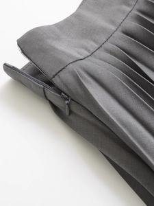 Macro detail of high-waist pleated skirt featuring side nylon zipper and woven texture