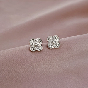 Macro shot of clover-shaped stud earrings with sparkling pavé crystals on pink silk
