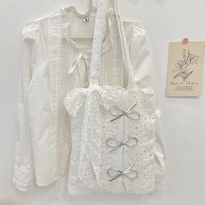 Detail of white lace tote bag featuring three silver bows and matching frilled shirt