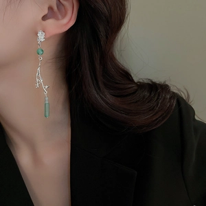 Detail of silver long drop earrings with green gemstones worn on ear for elegant style