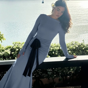 Detail view of the side pleats and black waist bow on this blue long sleeve dress