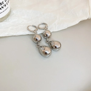 Polished silver geometric drop earrings displayed on minimalist textured background