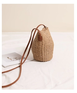 Detail of beige straw bucket bag with brown leather strap on white minimalist background