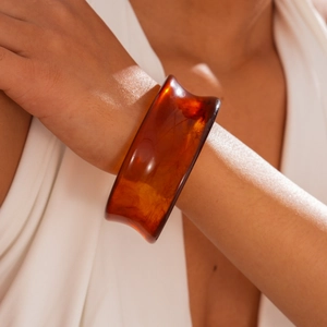 Close-up of a wide translucent amber resin bangle with natural marble textures and warm light