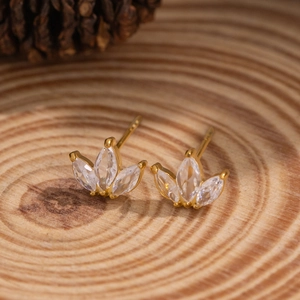 Close-up of golden petal studs with clear zircon stones on a natural wood texture background