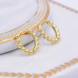 Detail of gold beaded hoop earrings with vintage texture on a ceramic display