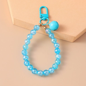 Detailed view of blue iridescent beaded charm with matching bell on beige stand