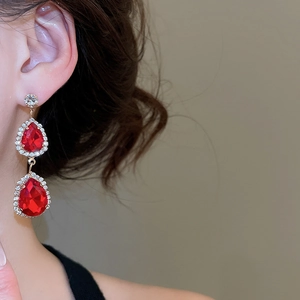 Detail of elegant gold drop earrings with red pear-cut stones and crystal halo on model