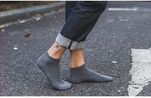 Detail of grey low-cut ribbed cotton socks worn with sneakers on an asphalt street