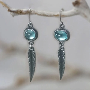 Macro detail of bohemian silver feather earrings featuring translucent sky blue stones