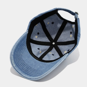 Detail view of denim baseball cap interior showing white daisy embroidery and reinforced tape