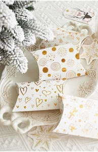 Macro detail of white pillow-shaped gift boxes with gold foil patterns on elegant tray
