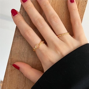 Hand wearing gold heart link ring set and thin textured band on wooden background