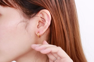 Close-up of polished gold-plated mini round hoop earrings worn on a model's earlobe
