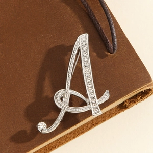 Elegant silver-toned letter A brooch with sparkling rhinestones on brown leather background