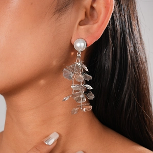 Close-up of silver leaf drop earrings with white pearl detail worn by a model