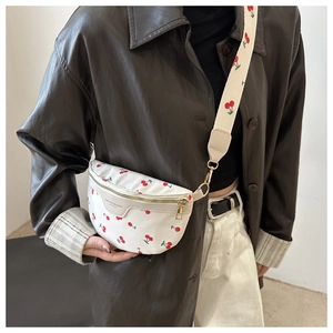 Close-up of white crossbody fanny pack with red cherry print and wide strap on model