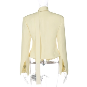 Rear view of cream blazer with scarf-style collar and slit cuffs on a clean backdrop