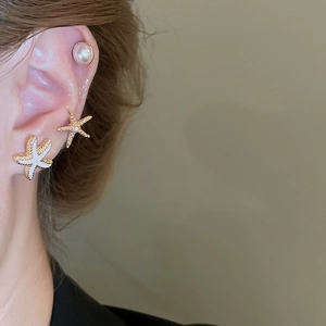 Detail of starfish and pearl stud earrings set in gold finish on female ear