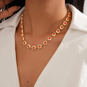 Close-up of a vintage golden necklace with oval red rhinestones worn on a white shirt